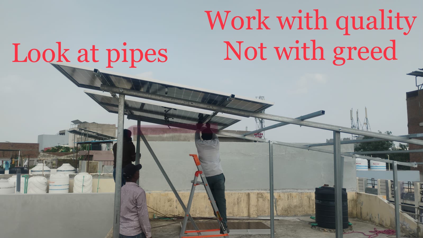 L K Solar Tech crew mounting panels on a galvanised rooftop structure, captioned "Work with quality, not with greed"
